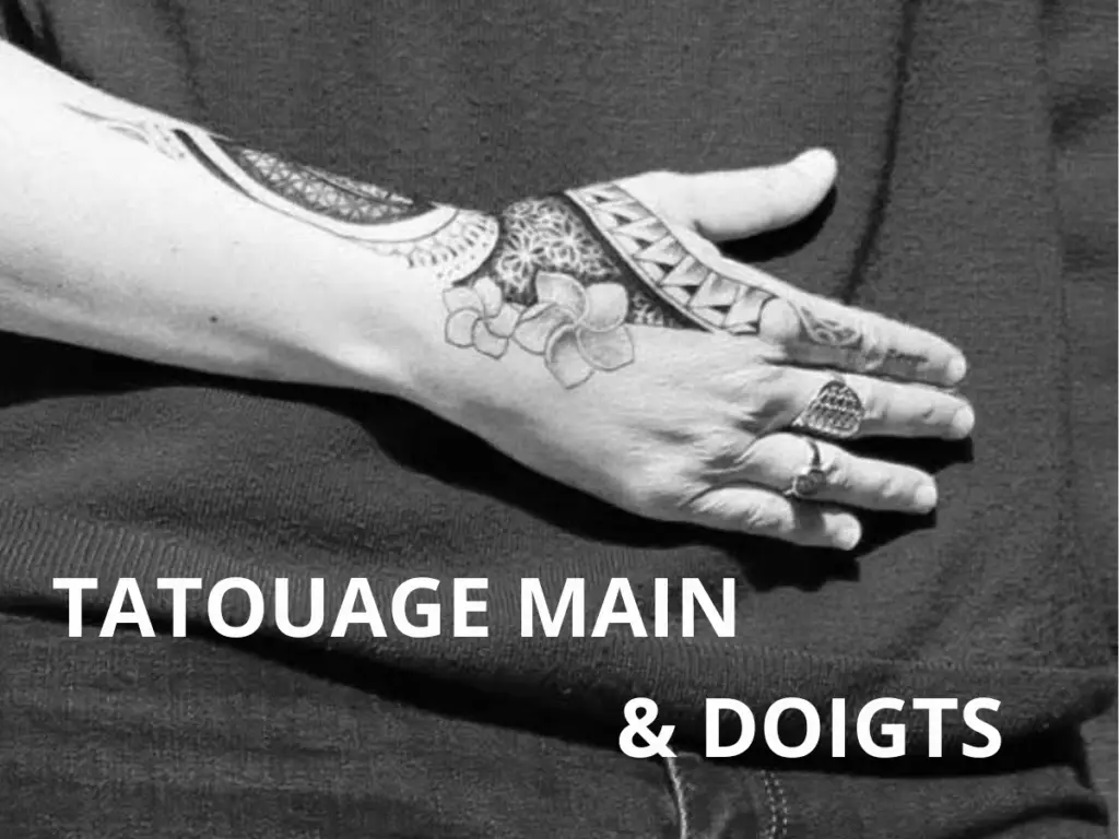Tatouage polynésien sur la main et les doigts, motif floral et géométrique, main posée sur un fond sombre, bijou sur les doigts.