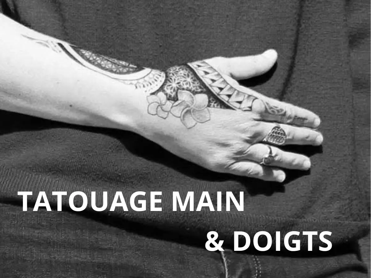 Tatouage polynésien sur la main et les doigts, motif floral et géométrique, main posée sur un fond sombre, bijou sur les doigts.