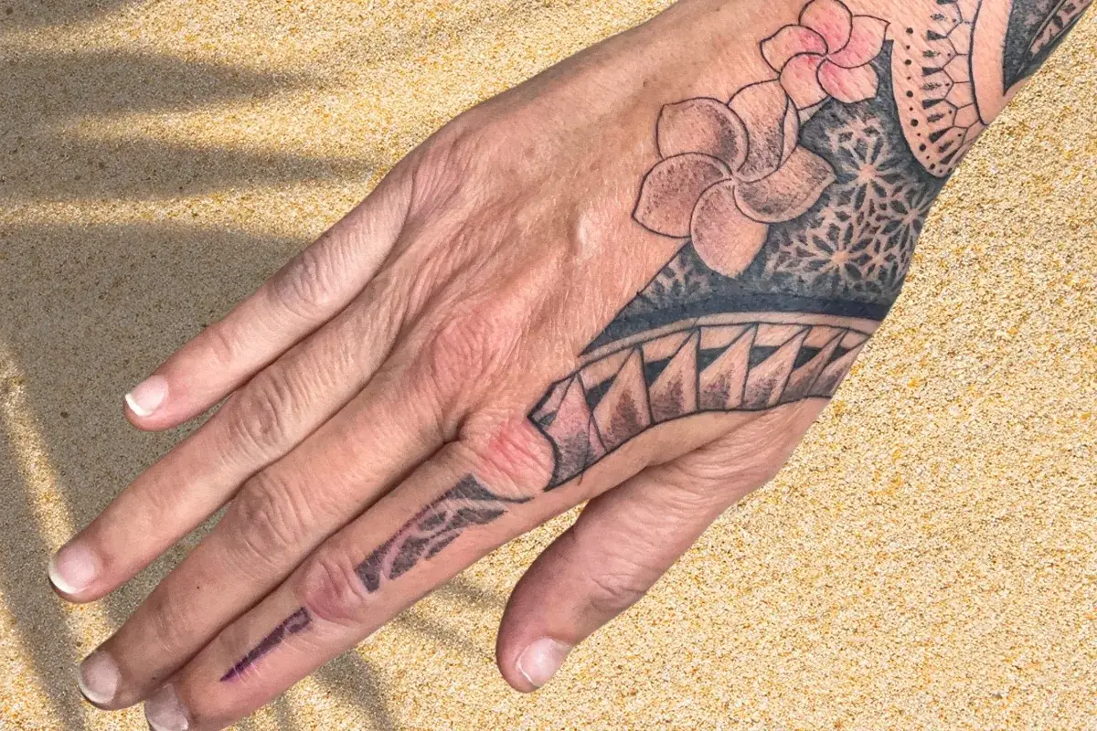 Tatouage polynésien complet sur main et doigt avec frangipaniers et motifs traditionnels mandala à Toulon Kanea