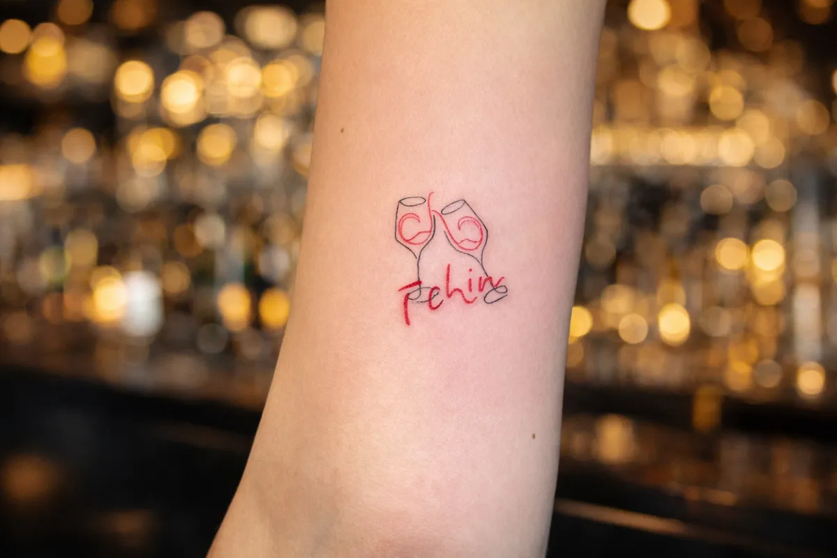 Tatouage minimaliste deux verres qui trinquent avec écriture sur le haut du bras Toulon Kanea