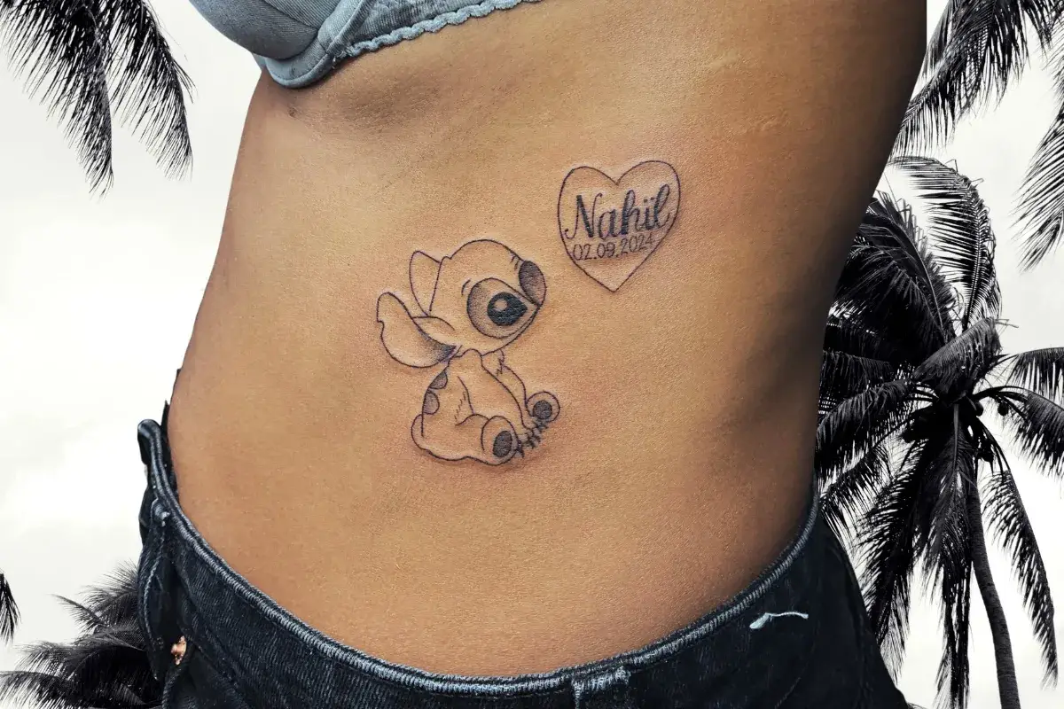Tatouage prénom Nahil avec personnage Disney Stitch et date dans un cœur sur le flanc à Toulon Kanea