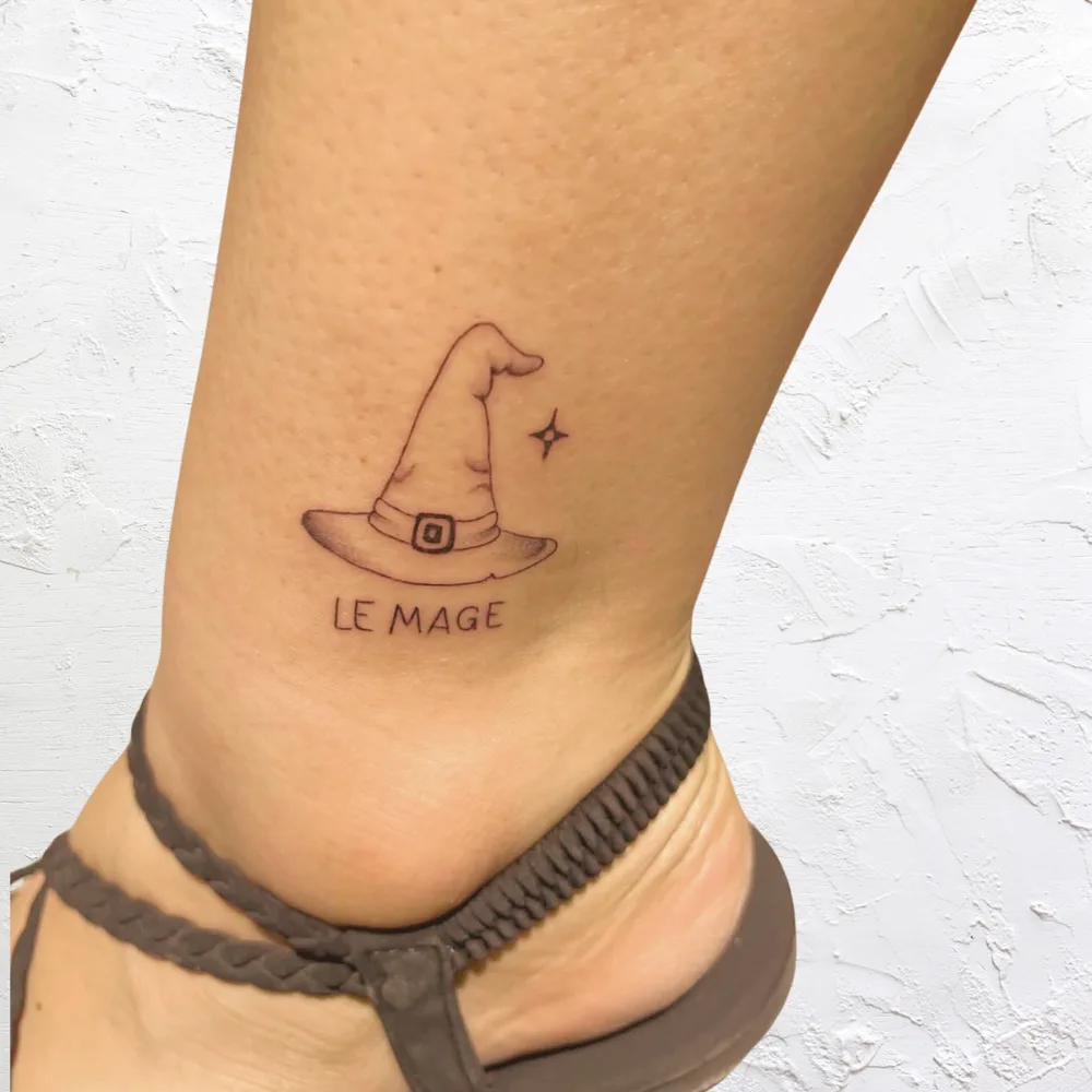 Tatouage fine line à la cheville : chapeau de mage avec une étoile et le mot Le Mage, Kanea Toulon