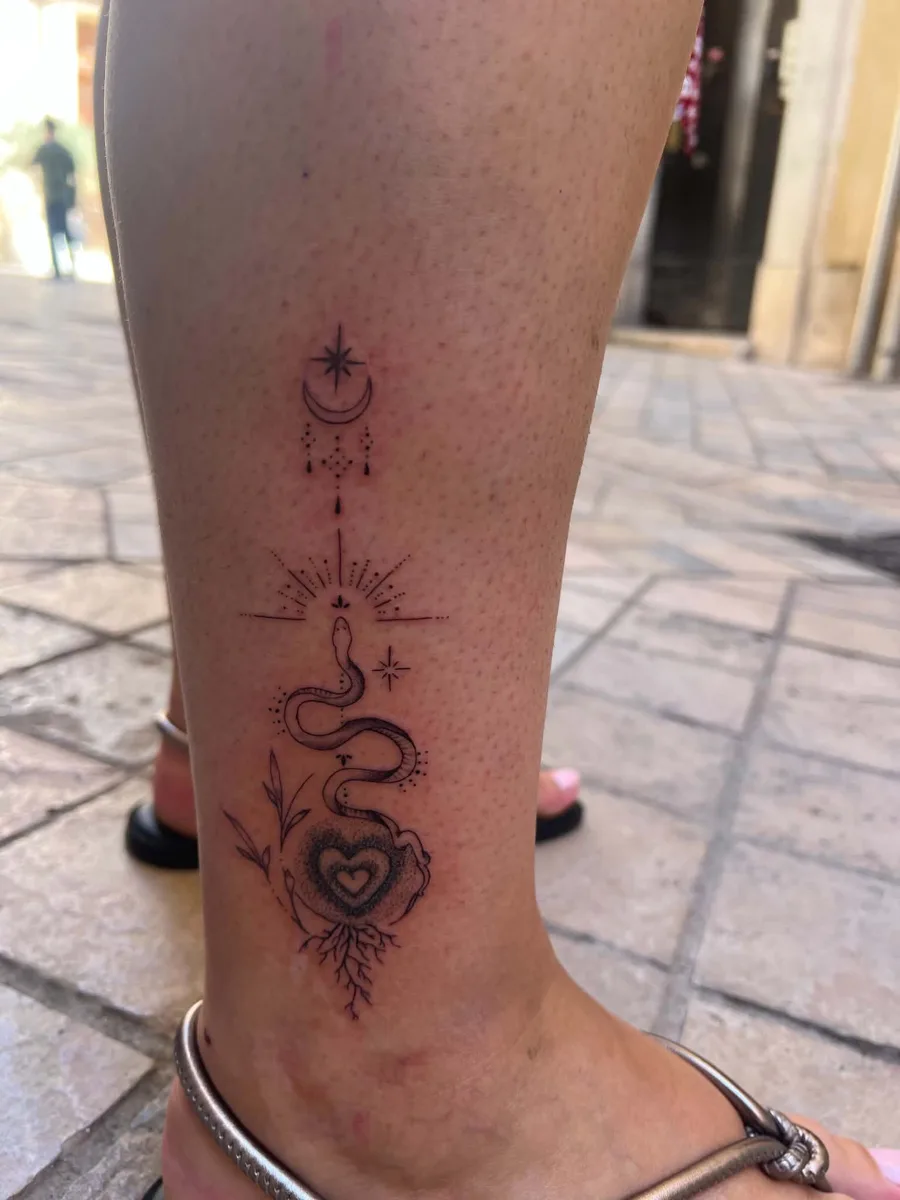 Tatouage fine line à la cheville : serpent enroulé autour d'un cœur en pointillés, racines, rayons, lune et étoile, Kanea Toulon